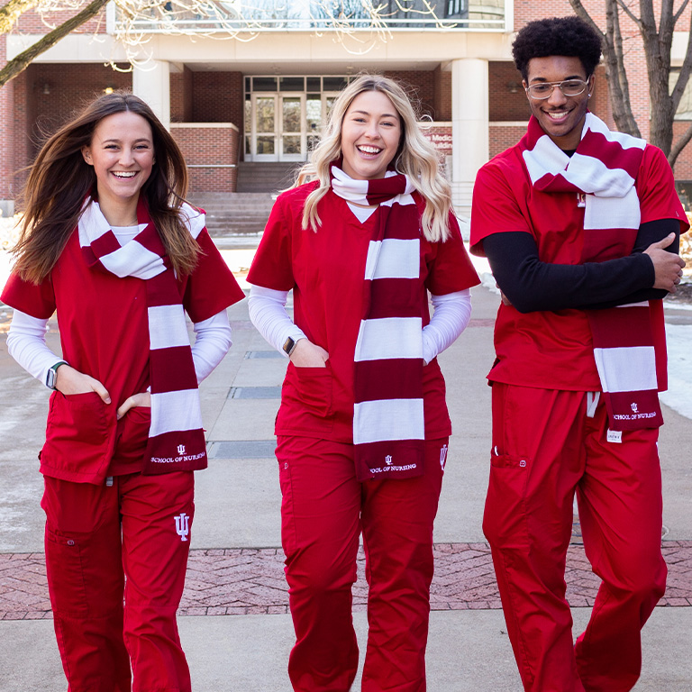 Three IU Indianapolis nursing students walk outside the School of Nursing building in red-and-white scarves