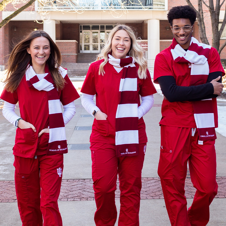 Three IUPUI nursing students walk outside the School of Nursing building in red-and-white scarves