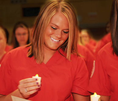 Nursing students in red scrubs holding candles