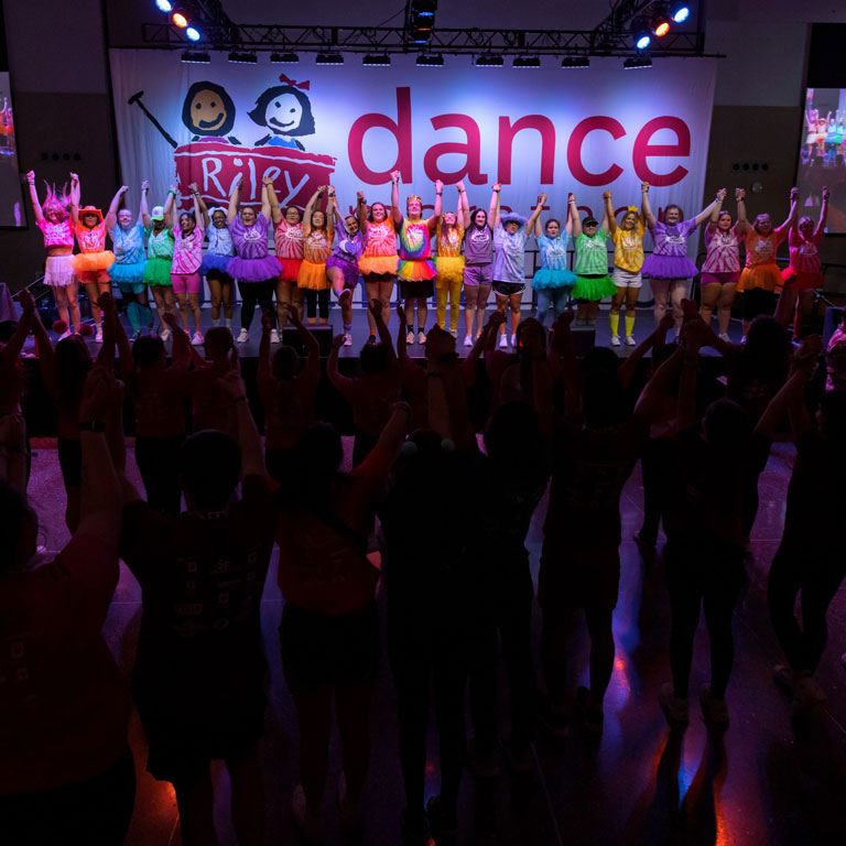 Students stand on the Jagathon Dance Marathon stage with raised hands clasped during the 2024 event