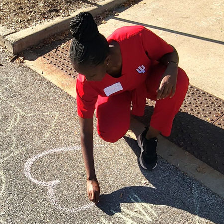 Moi University student Olivia Watta draws a heart with chalk on a sidewalk at IU Bloomington.