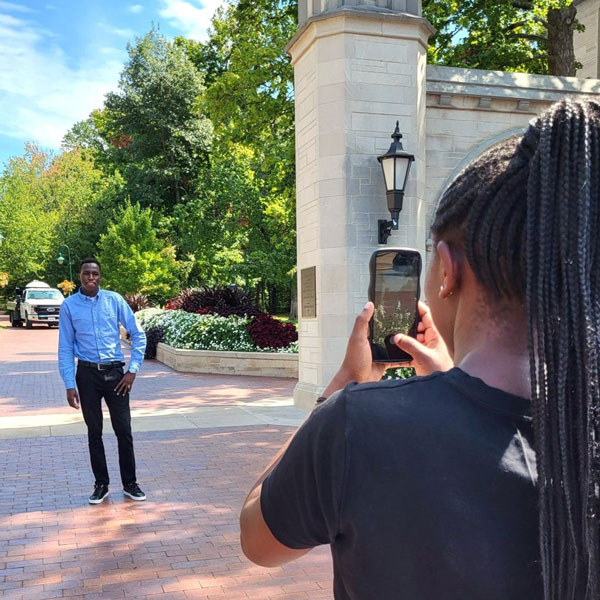 Moi University student Olivia Watta takes a photo of Moi University student Victor Kiplagat at IU Bloomington's Sample Gates.