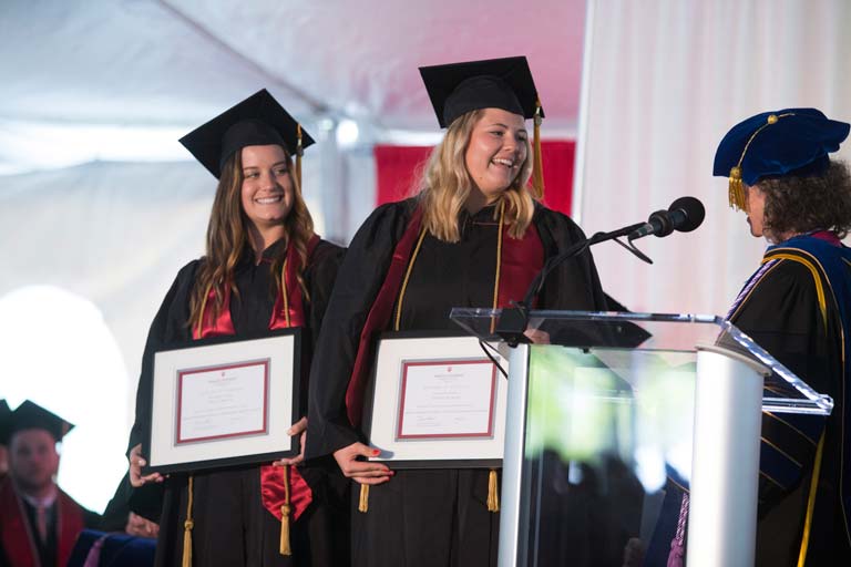 Two graduates holding awards
