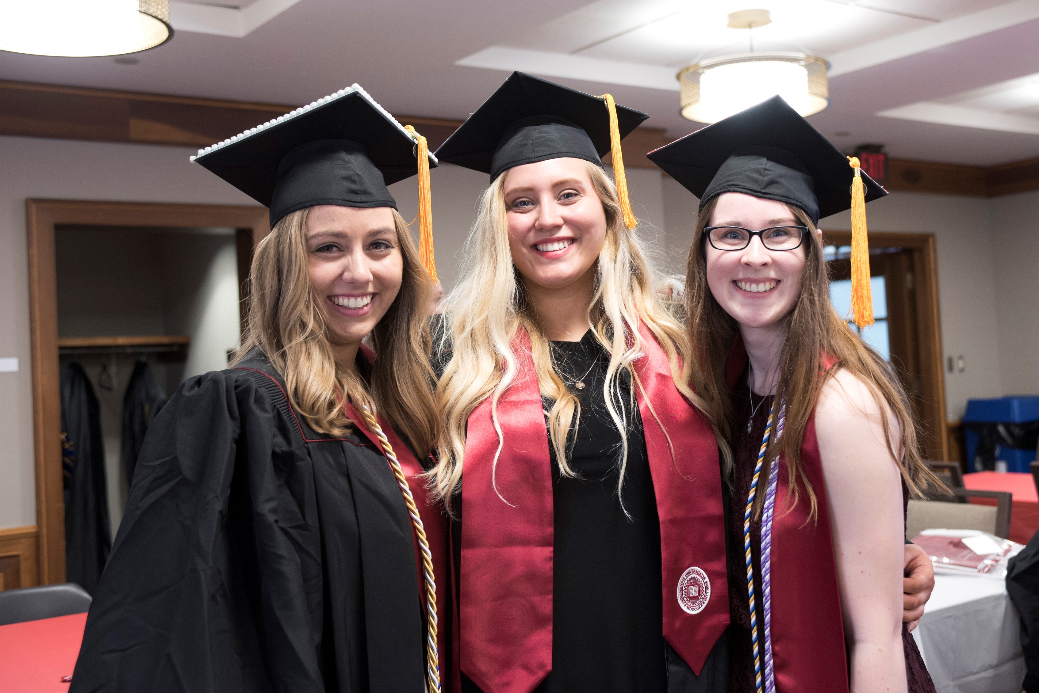 Three students in caps and gowns smiling at camera