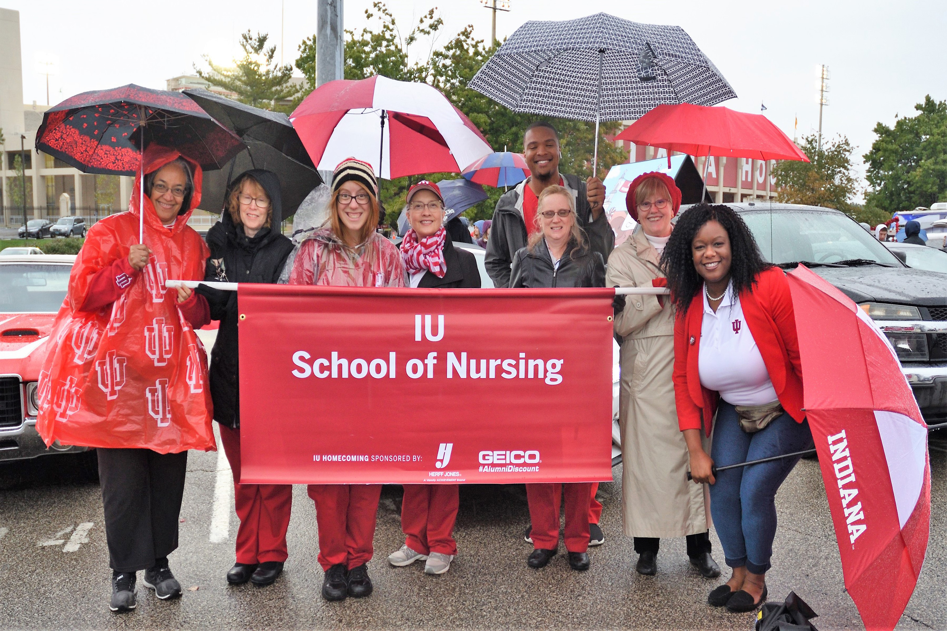 fans in rain gear and holding sign at rainy homecoming parade