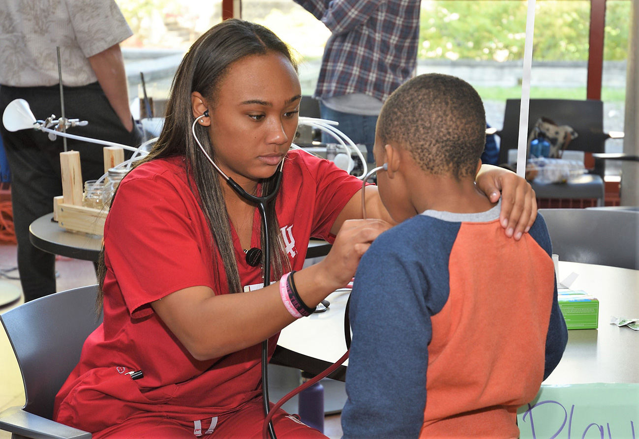 Child and student nurse listen through stethoscopes at Science Fest