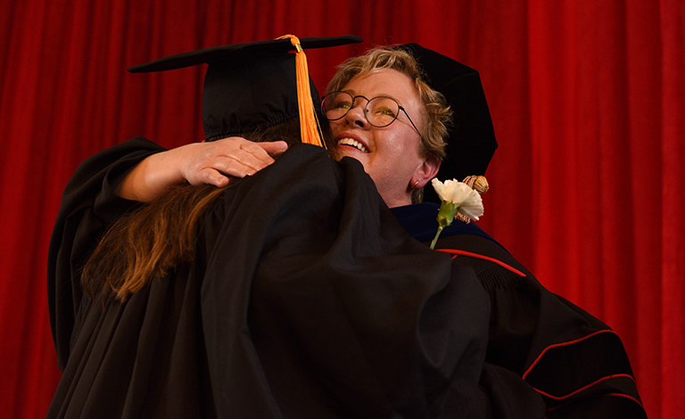 A graduate and faculty hugging