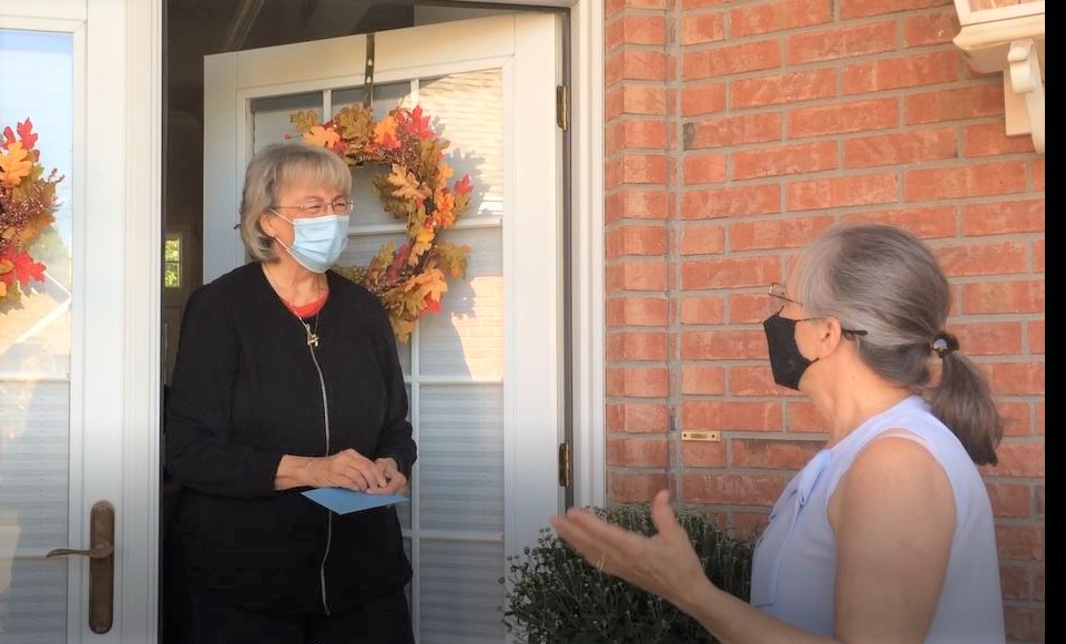 Woman greets another woman at an open door of a home