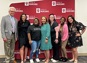 A group of people pose for a photo in front of a red Indiana University School of Nursing background