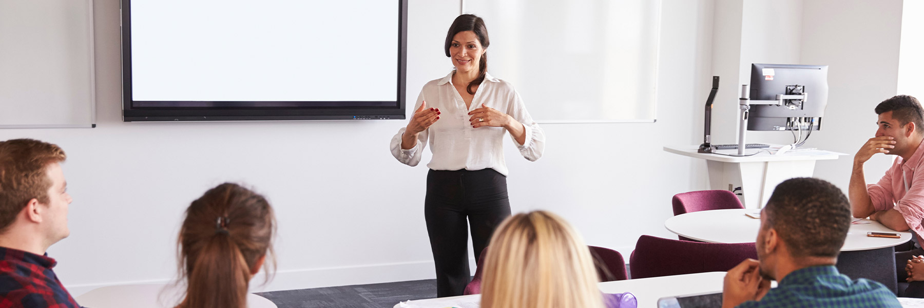 Woman standing in front of a white board talking to a group of people